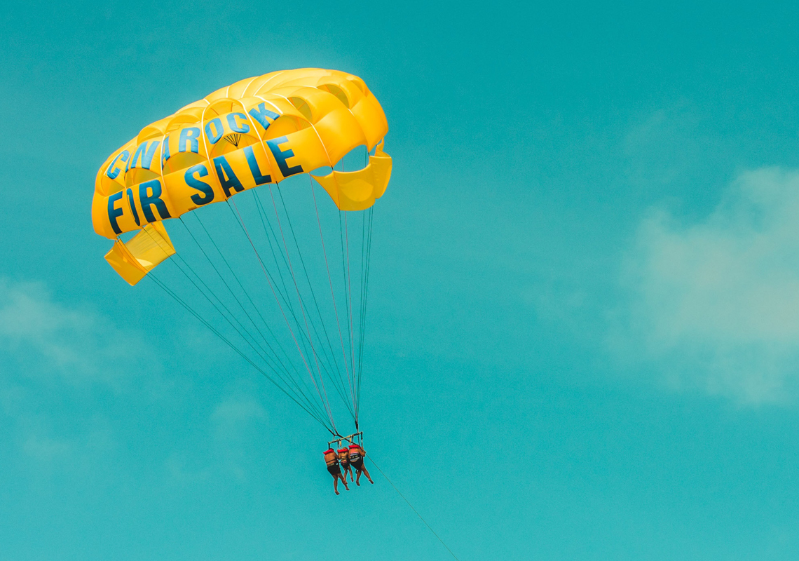 couple floating in a parachute with for sale written on