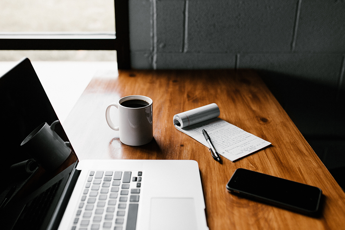 macbook, coffee, pen, pag and phone on wooden table