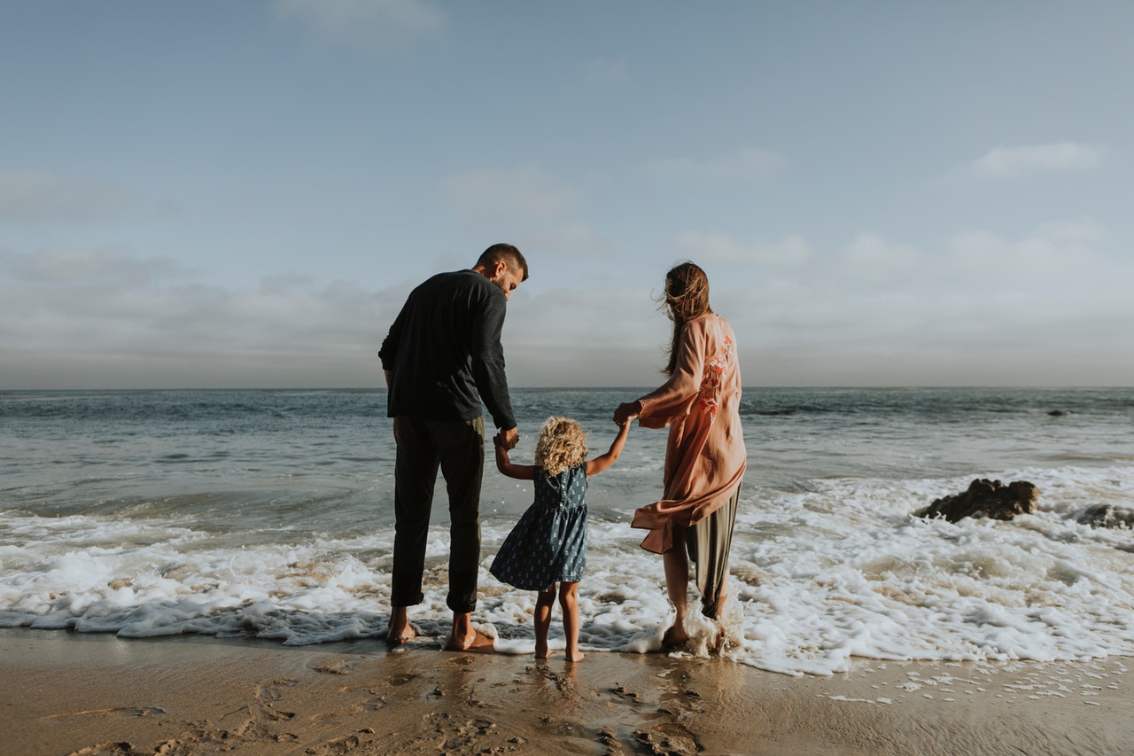 family of 3 dipping their feet in the sea on a sunny day