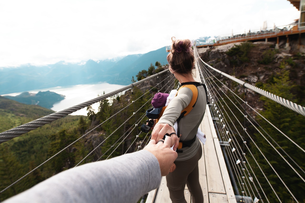 woman holding mans hand leading him across a bridge